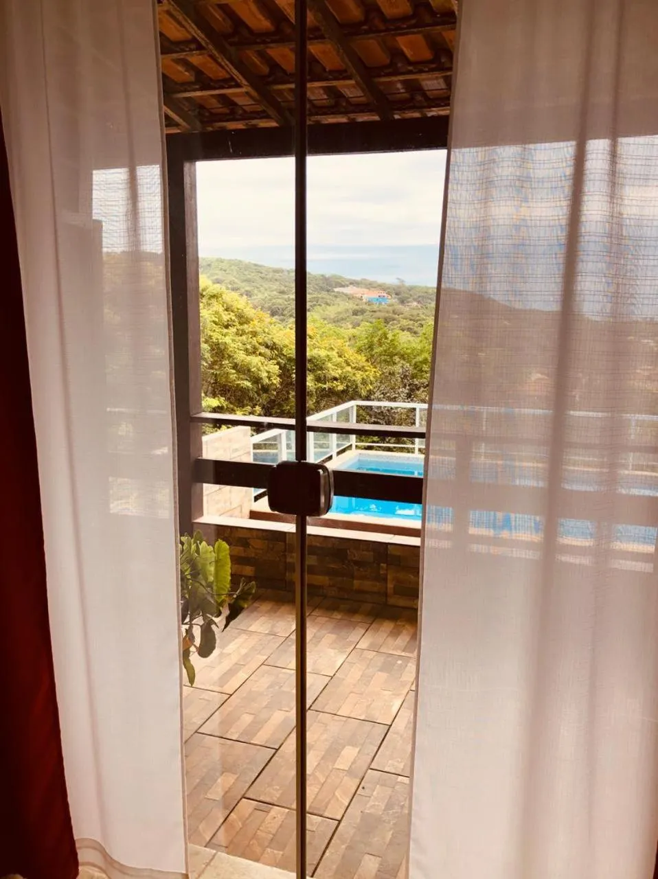 Vue sur une piscine et la mer depuis un balcon ombragé.