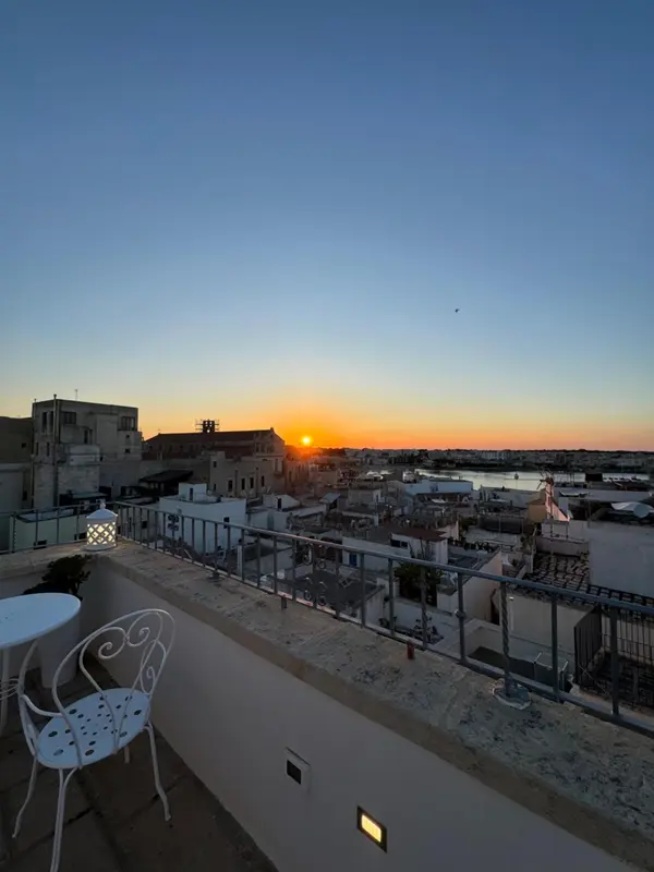 Terrasse avec mobilier blanc dominant un paysage urbain au coucher du soleil.
