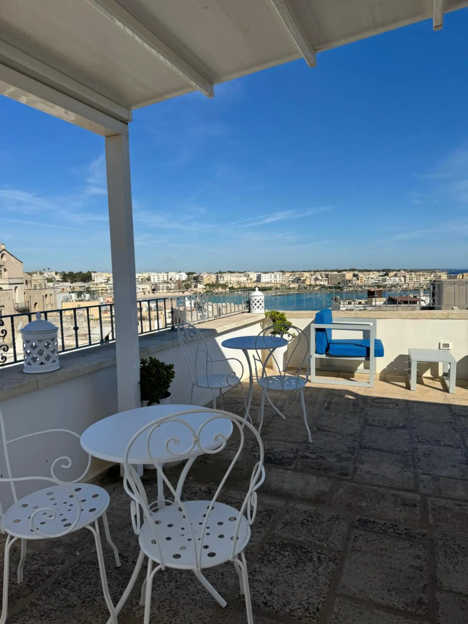 Terrasse avec mobilier blanc offrant une vue sur la mer et la ville.
