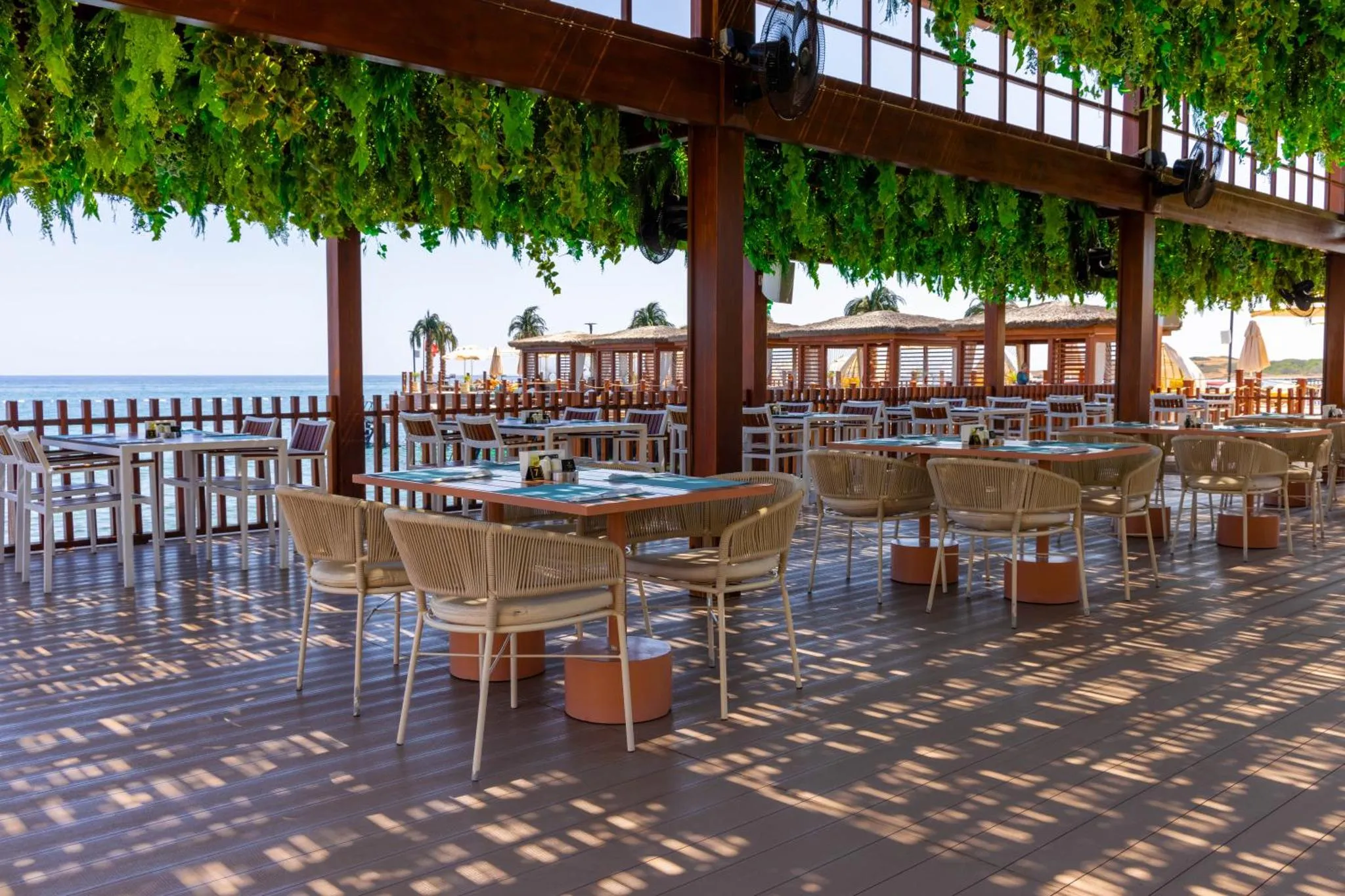 Terrasse ombragée avec tables et chaises en bord de mer.