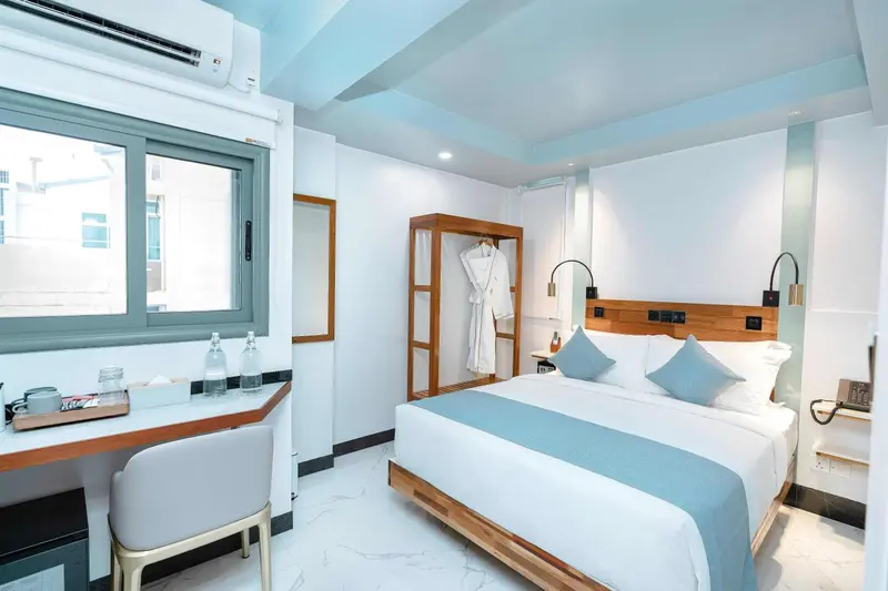 Une chambre lumineuse avec un grand lit et un bureau près de la fenêtre.