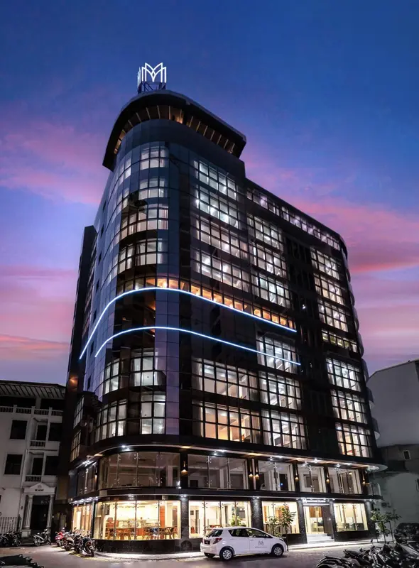 Bâtiment moderne illuminé au crépuscule avec une façade incurvée et de nombreuses fenêtres.