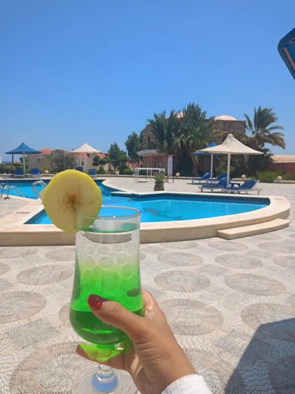 Un cocktail coloré sur une terrasse ensoleillée avec une piscine en arrière-plan.