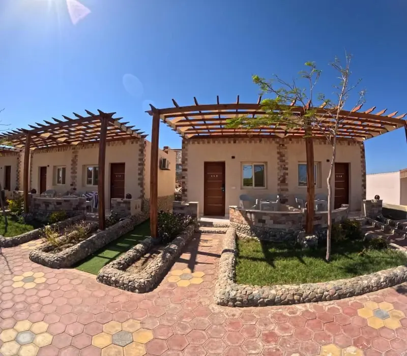 Petites maisons beiges avec des pergolas en bois et des jardins soignés.