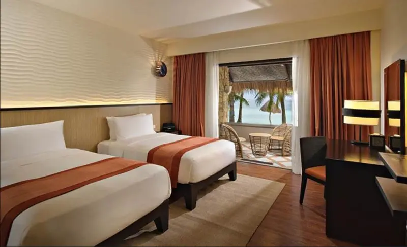 Chambre avec deux lits et vue sur une terrasse en bord de mer.