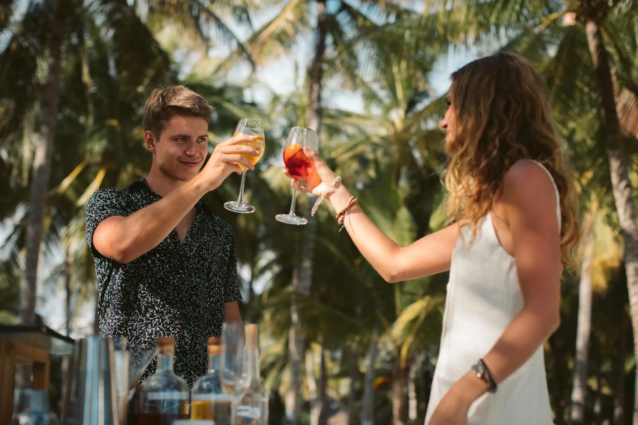 Un couple trinque avec des verres colorés sur une terrasse ensoleillée.
