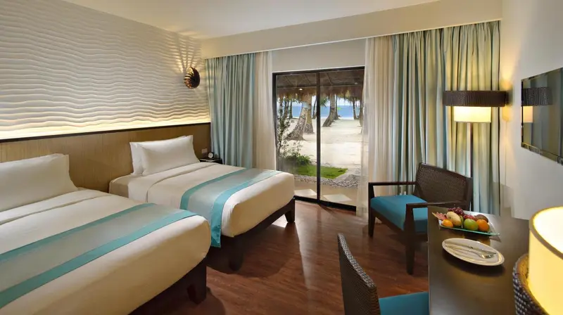Chambre lumineuse avec deux lits et vue sur la plage.