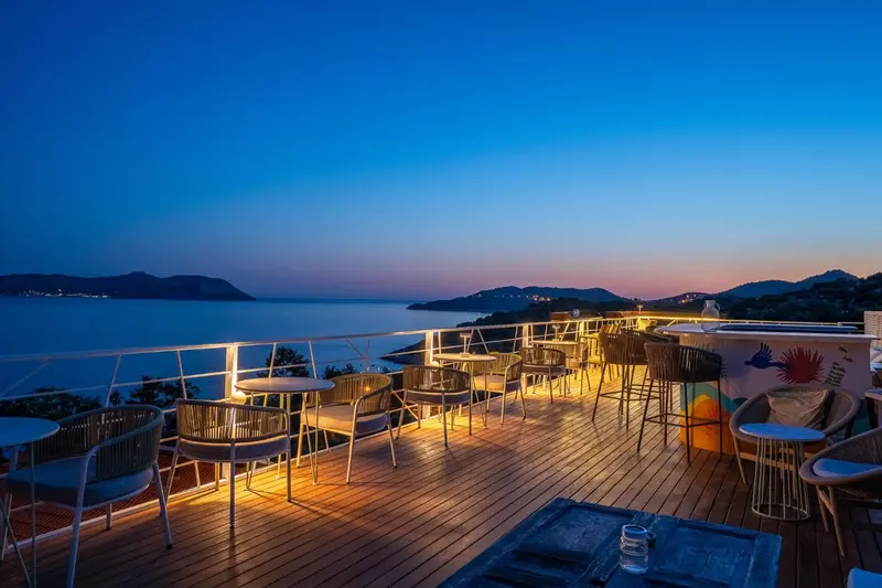 Terrasse lumineuse avec tables et chaises donnant sur une vue nocturne de la mer.
