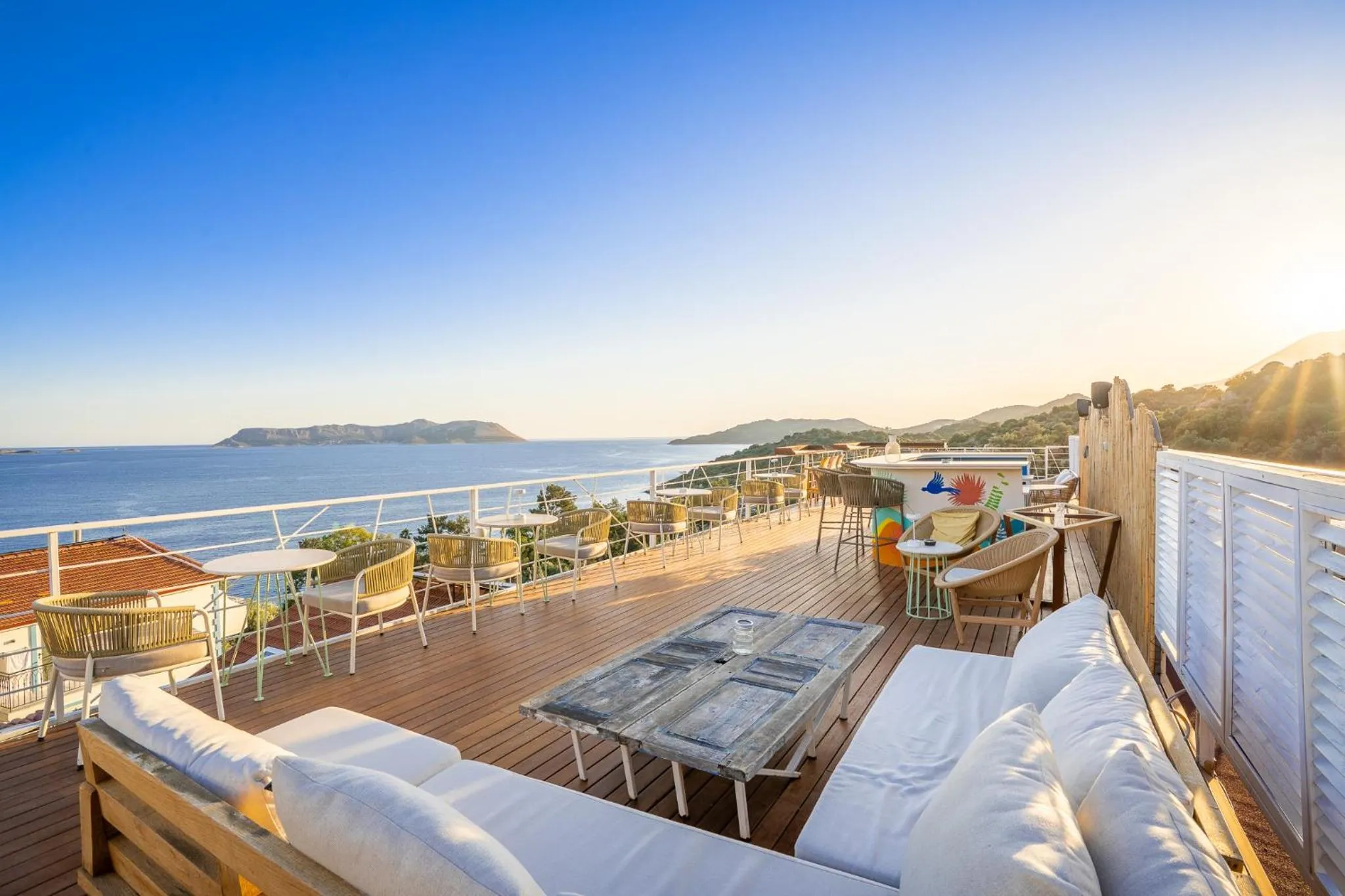 Terrasse aménagée avec canapés, tables et chaises offrant une vue sur la mer et les collines.