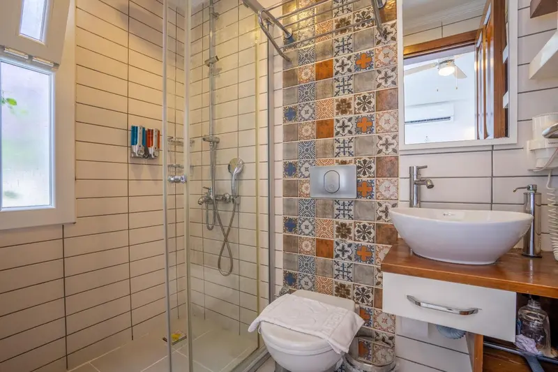 Une douche à l'italienne avec des carreaux décoratifs et un lavabo sur un meuble en bois.