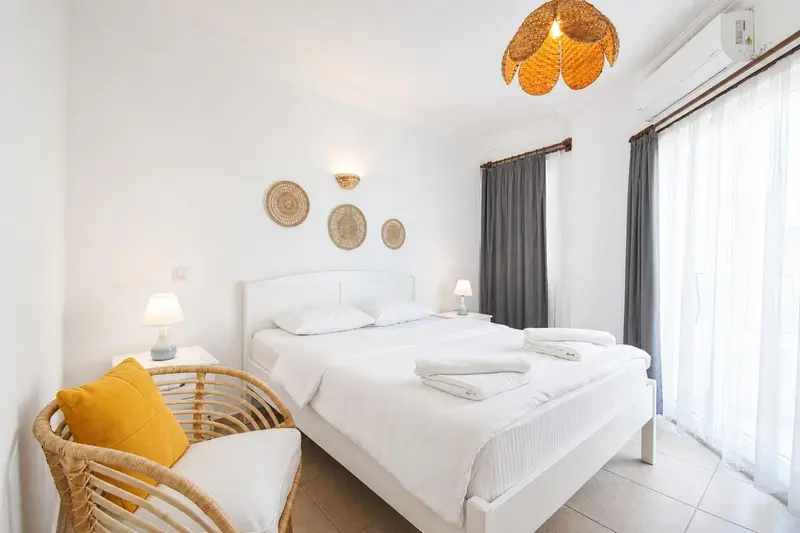 Une chambre lumineuse avec un lit blanc et une décoration murale en rotin.