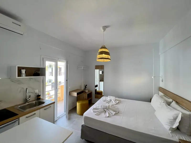 Une chambre lumineuse avec un lit fait et un coin cuisine.