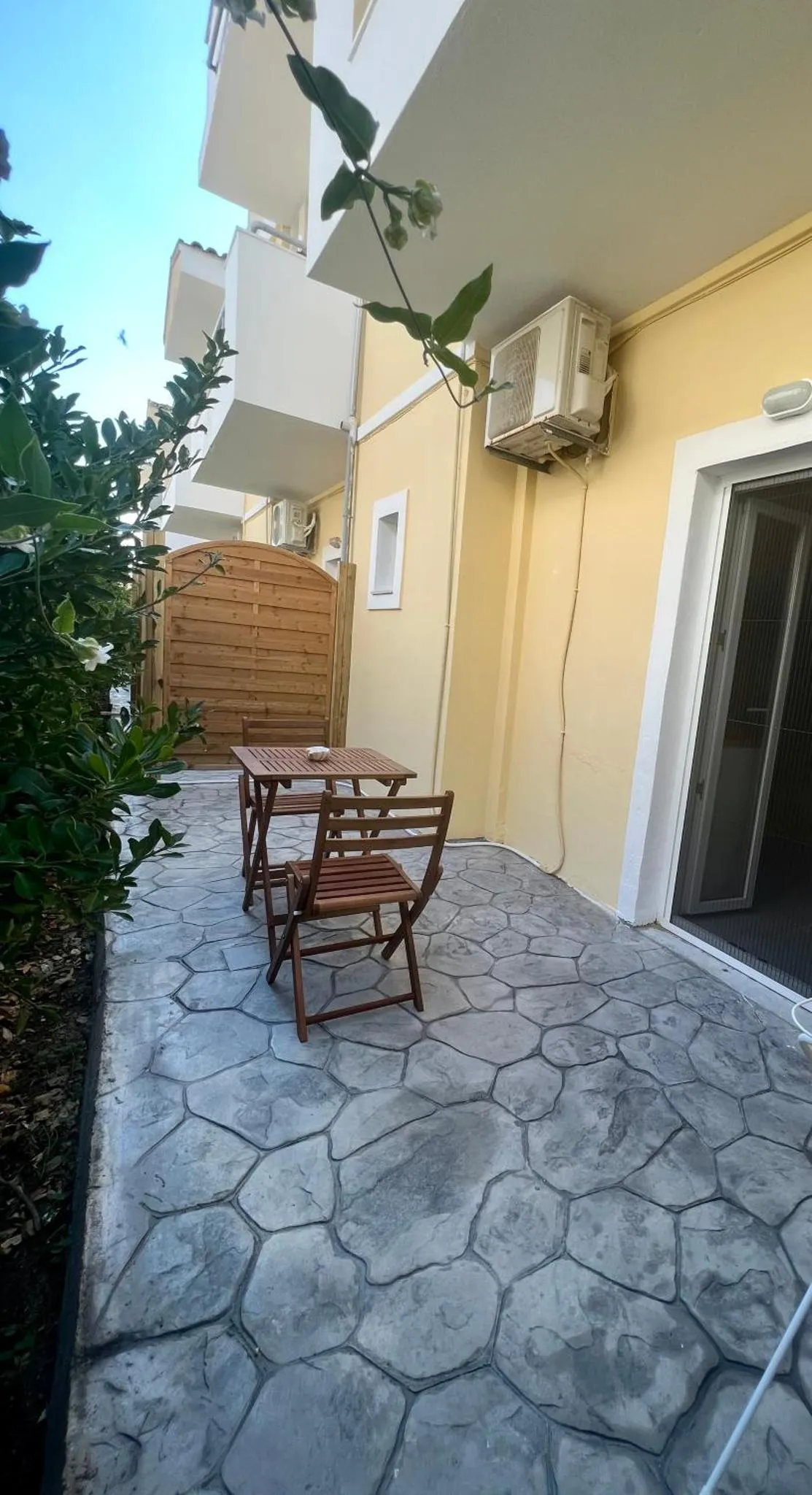 Une petite terrasse avec une table et des chaises en bois se trouve devant un mur jaune.