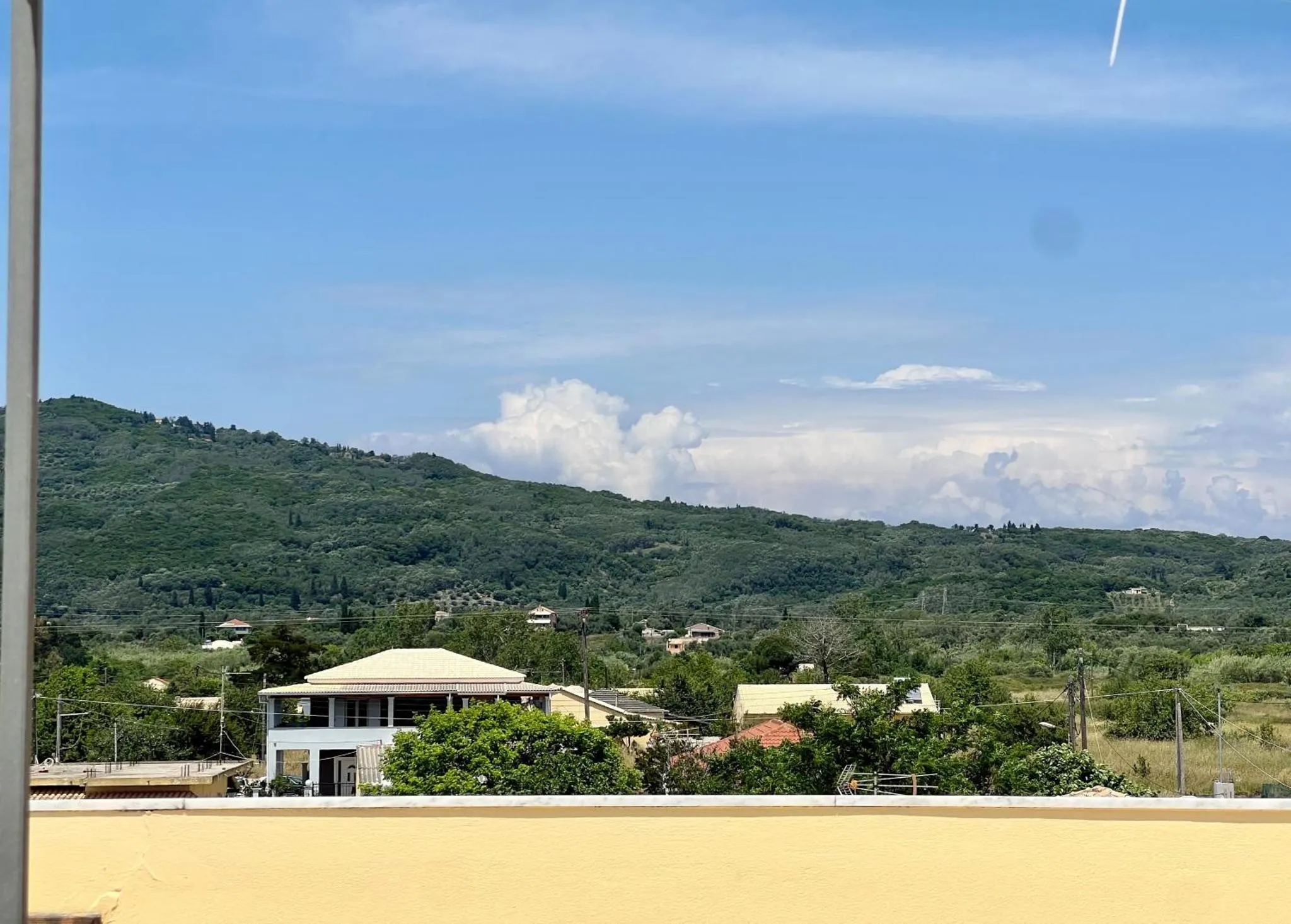Paysage de collines verdoyantes et d'une maison blanche sous un ciel nuageux.