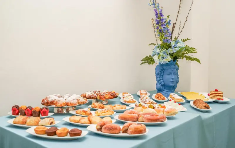 Une table recouverte d'une nappe turquoise présente une variété de pâtisseries et de fruits.