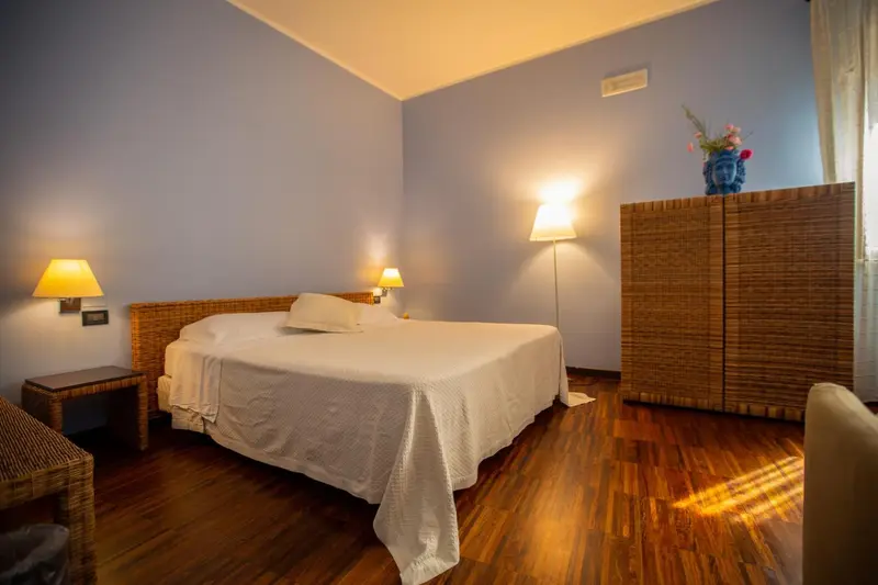 Une chambre lumineuse avec un lit recouvert d'une couverture blanche et des meubles en rotin.