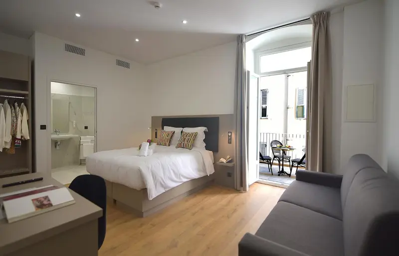 Une chambre lumineuse avec un lit double et un canapé, donnant sur un balcon.