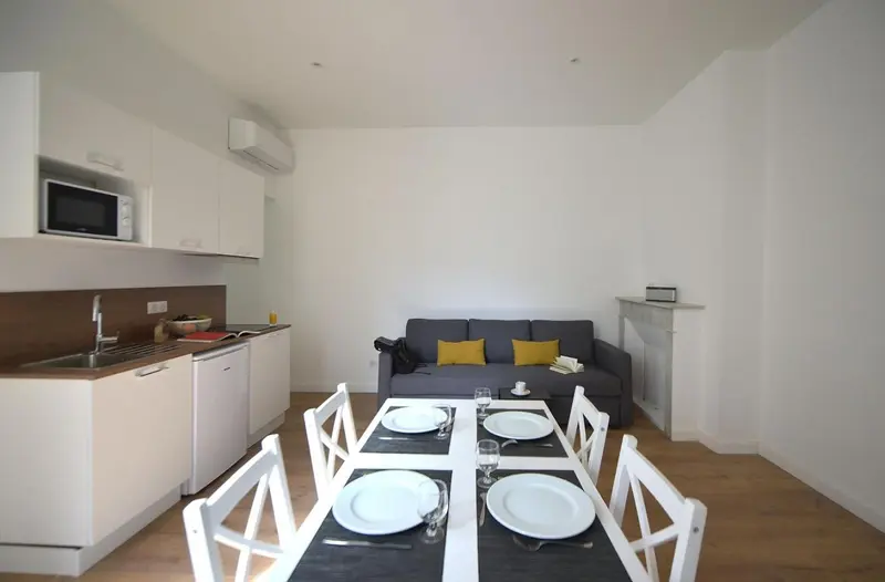Une table est dressée dans une pièce lumineuse avec un canapé et une kitchenette.