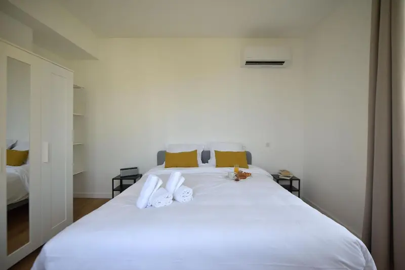 Une chambre lumineuse avec un grand lit recouvert d'une courtepointe blanche et de coussins colorés.