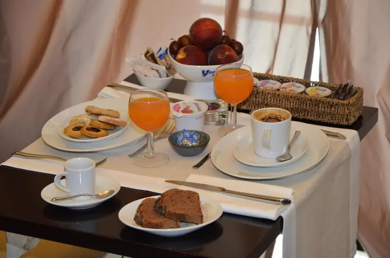 Une table est dressée avec un petit-déjeuner composé de viennoiseries, de fruits et de boissons.