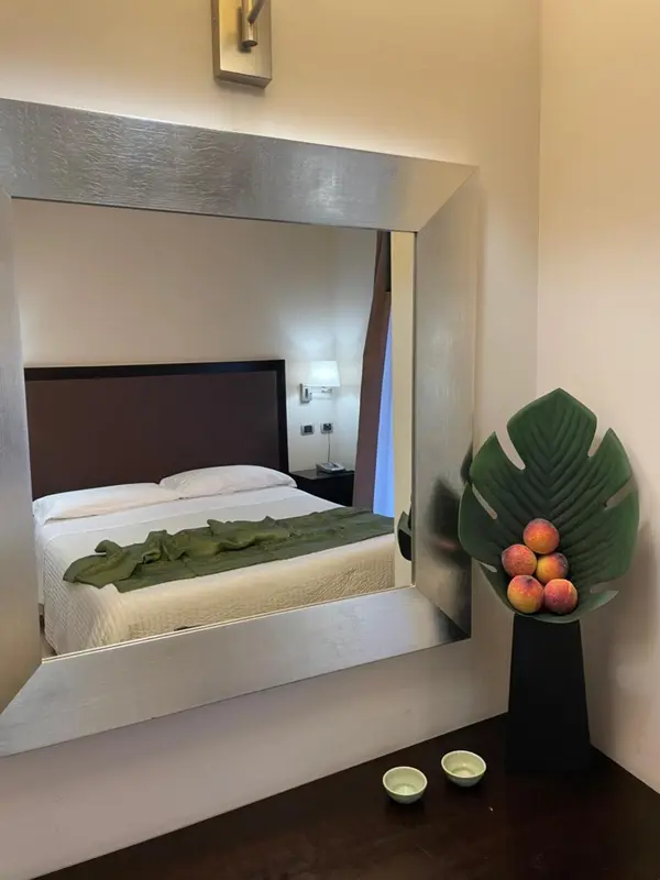 Une chambre avec un lit recouvert d'une couverture verte et un grand miroir.