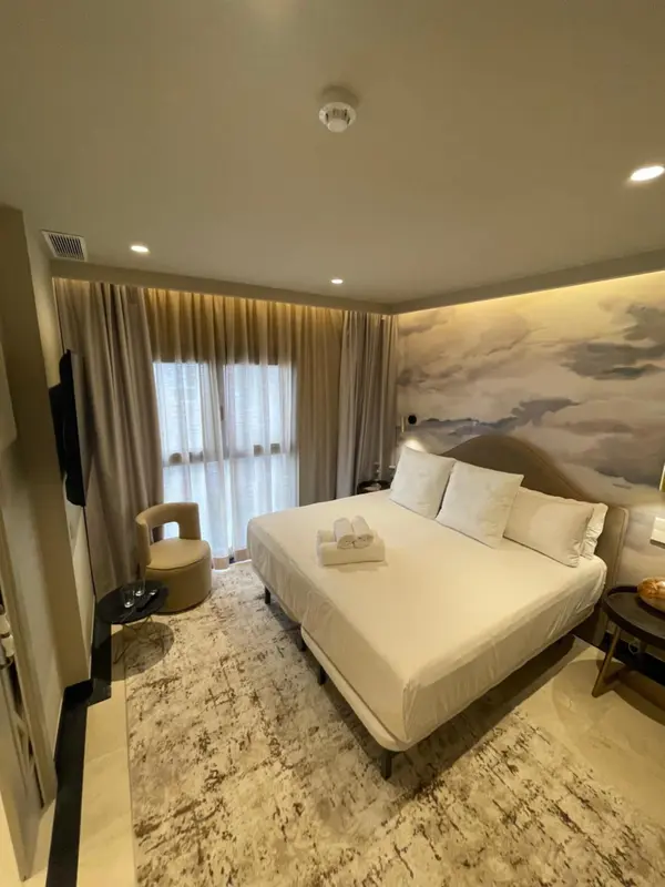 Une chambre lumineuse avec un grand lit et un décor mural évoquant un paysage marin.