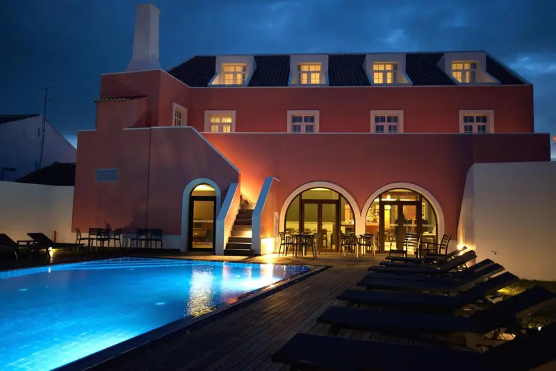 Bâtiment rose éclairé avec une piscine au premier plan.