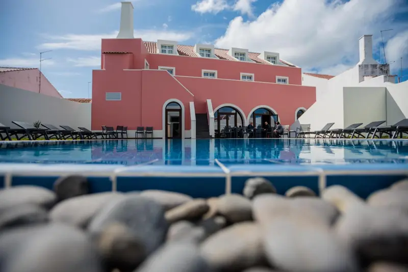 Bâtiment rose avec piscine et chaises longues au premier plan.
