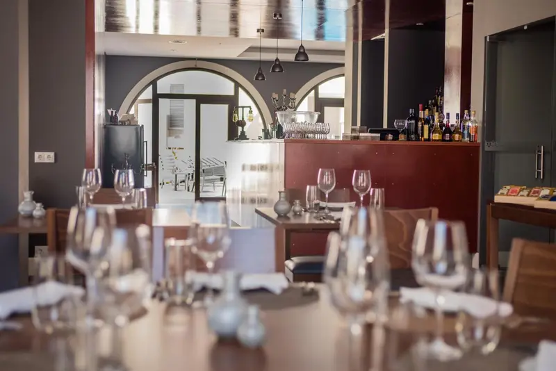 Une salle de restaurant avec des tables dressées et un comptoir de bar en arrière-plan.
