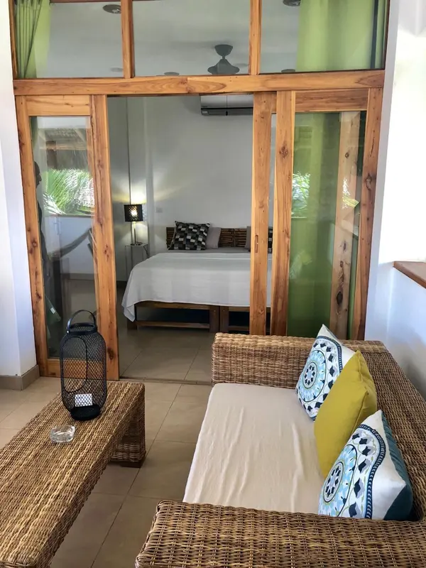 Espace de détente avec canapés en rotin et vue sur une chambre à coucher.