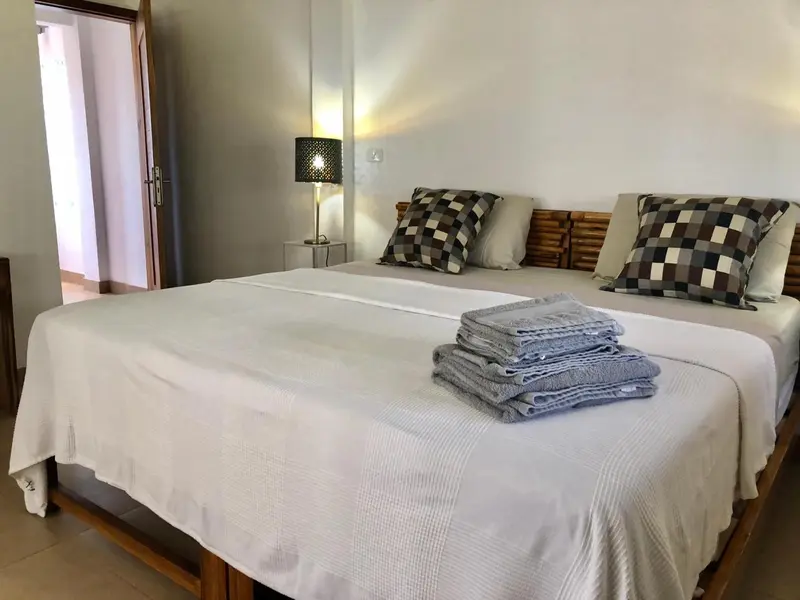 Une chambre lumineuse avec un grand lit recouvert d'une courtepointe blanche et de coussins.