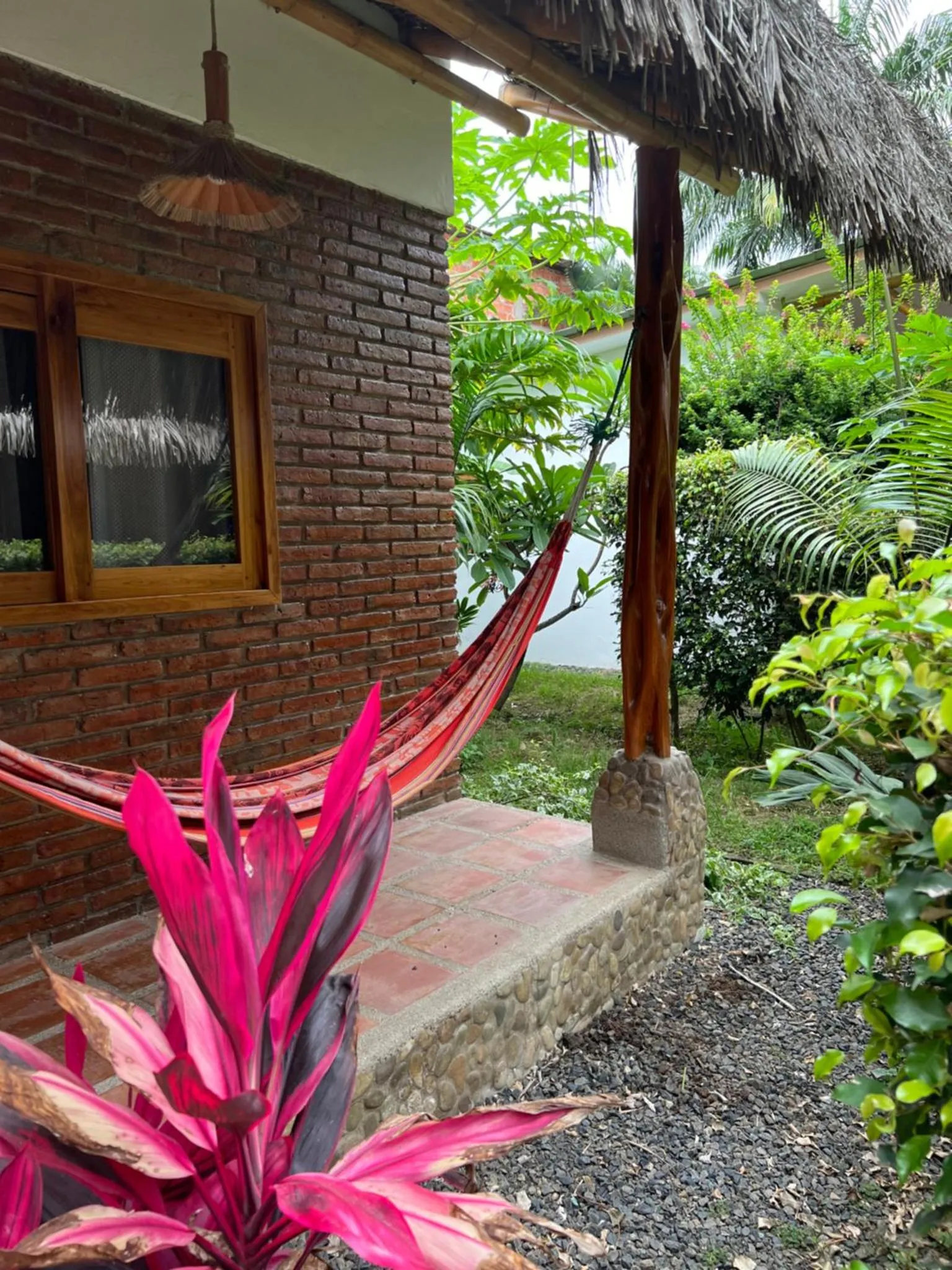 Une terrasse ombragée avec un hamac rouge et des plantes tropicales.