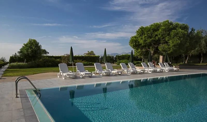 Transats blancs alignés au bord d'une piscine turquoise sous un ciel bleu.