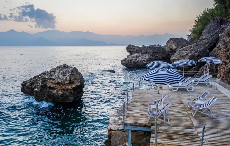 Plateforme en bois avec transats bleus et parasols rayés au bord de la mer.