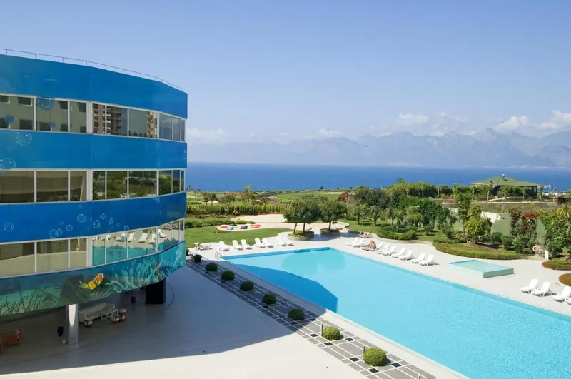 Vue aérienne d'un bâtiment bleu moderne avec une piscine et un paysage marin en arrière-plan.