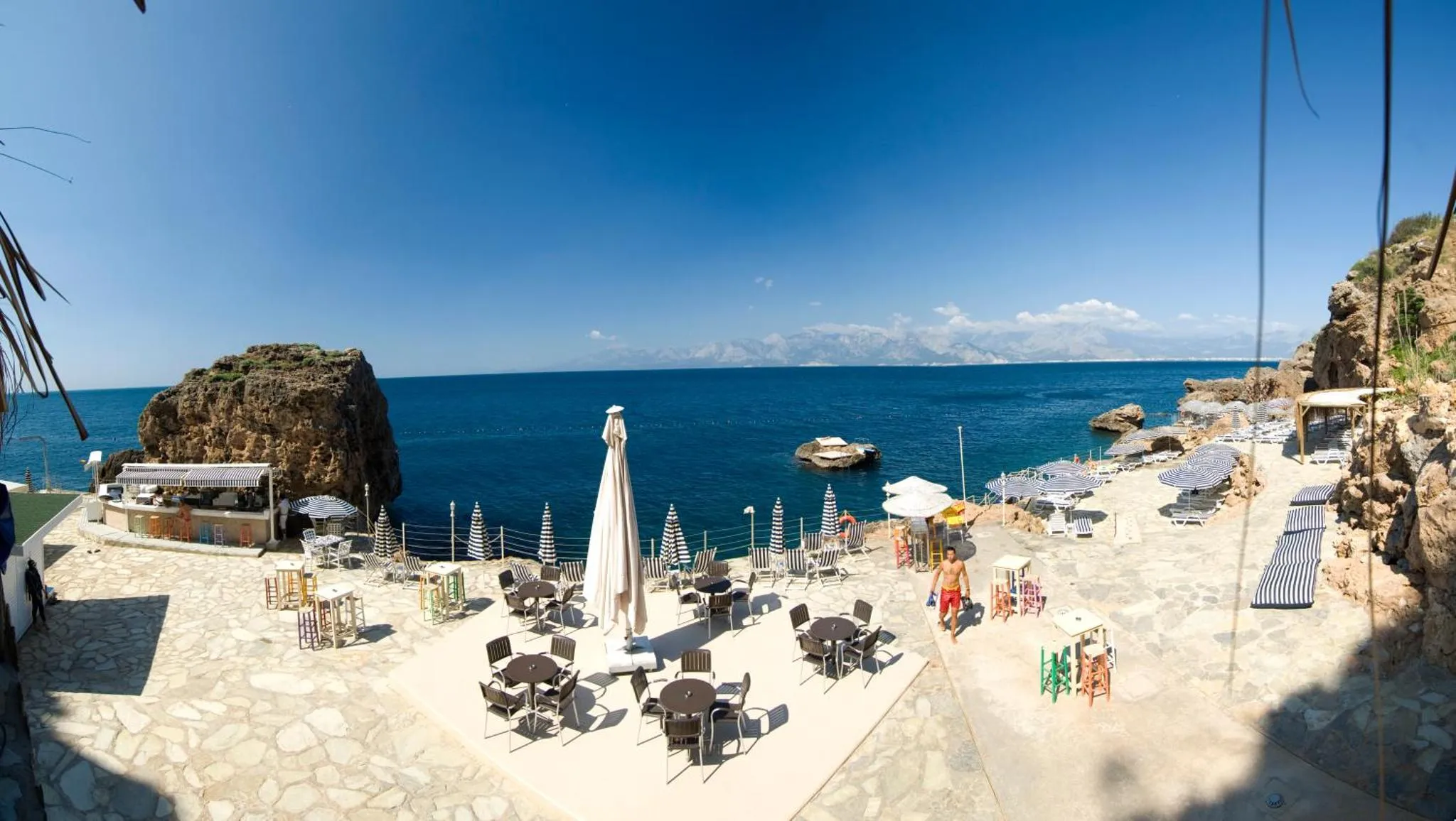 Terrasse ensoleillée avec tables et chaises face à la mer.