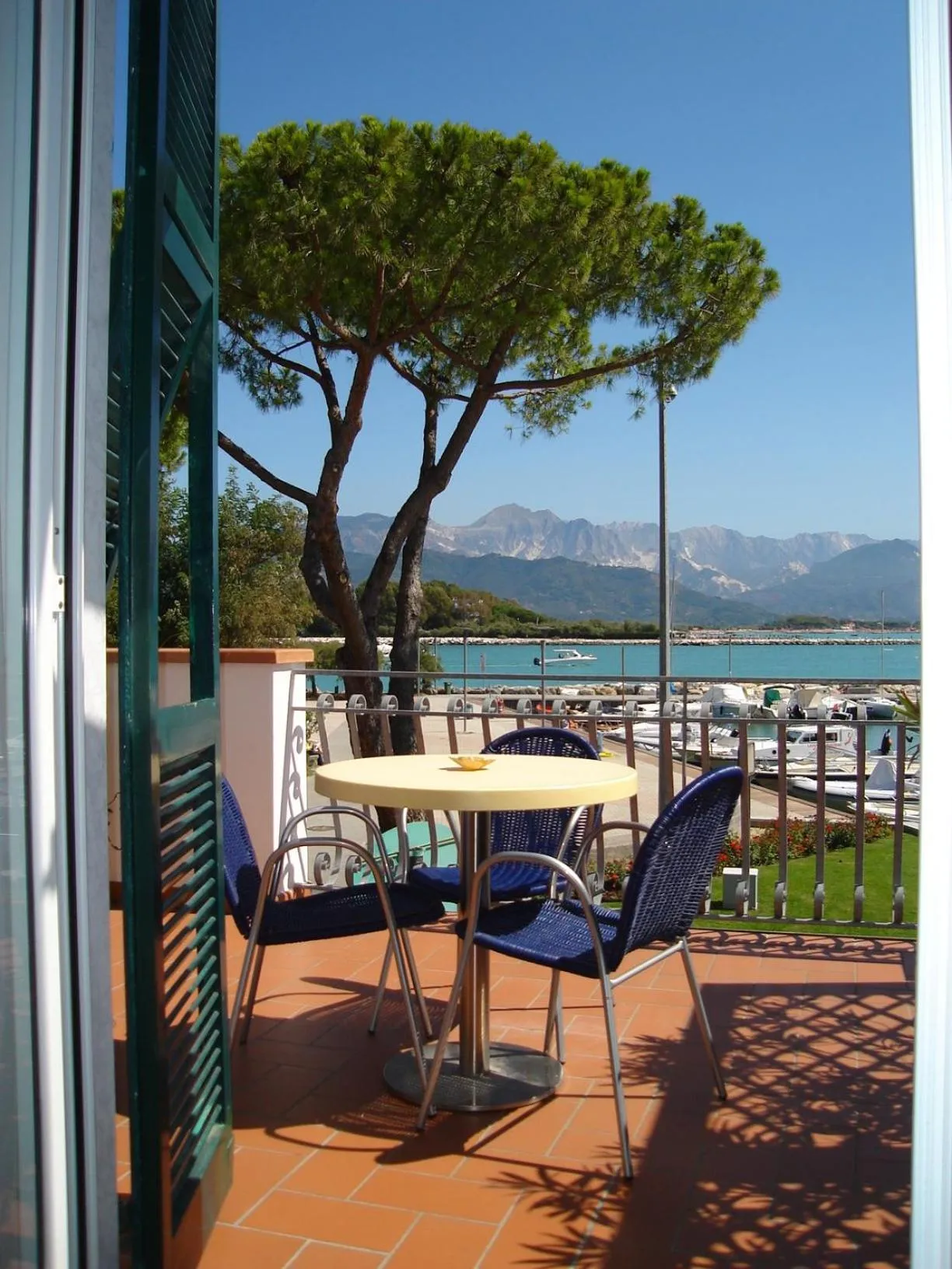 Une table ronde et des chaises en osier sur une terrasse carrelée offre une vue sur la mer et les montagnes.