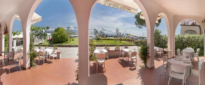 Terrasse ombragée avec tables et chaises donnant sur un paysage côtier.