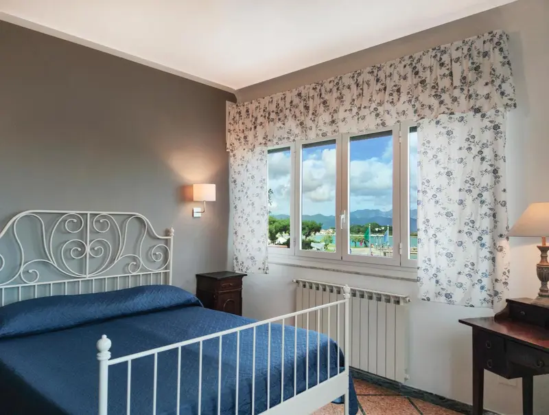 Une chambre lumineuse avec un lit en fer forgé et une vue sur un paysage verdoyant.