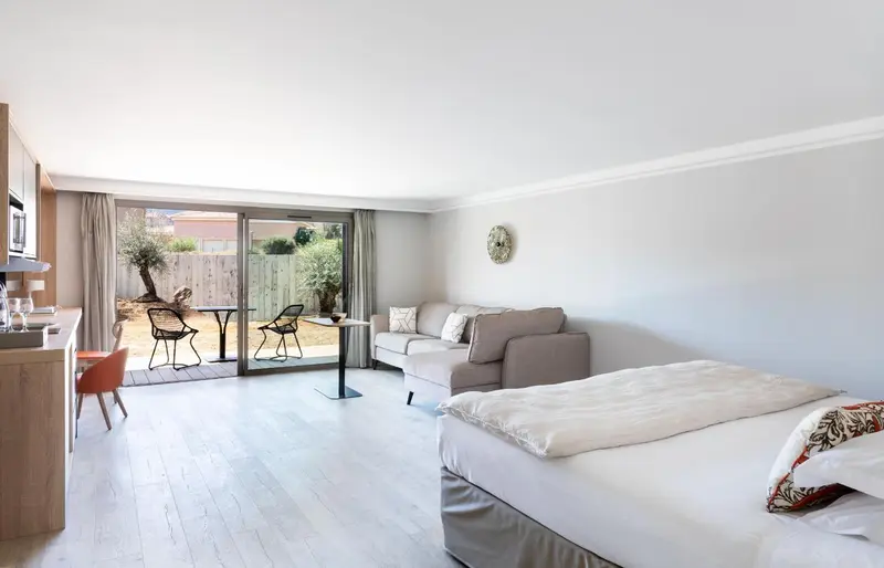 Espace de vie lumineux avec canapé, lit et accès à une terrasse.