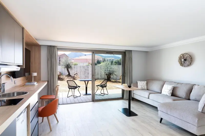 Interieur lumineux avec coin cuisine, espace salon et terrasse donnant sur un jardin.