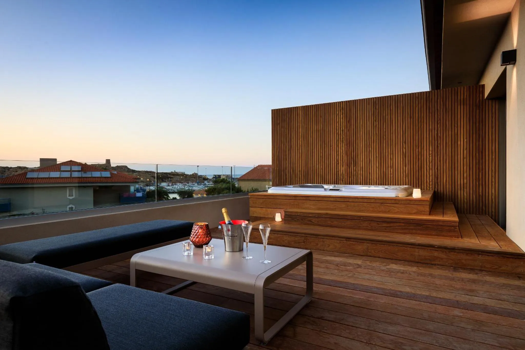 Terrasse avec salon et jacuzzi offrant une vue sur la mer et le ciel crépusculaire.