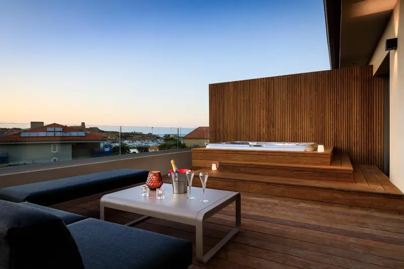 Terrasse avec salon et jacuzzi offrant une vue sur la mer et le ciel crépusculaire.