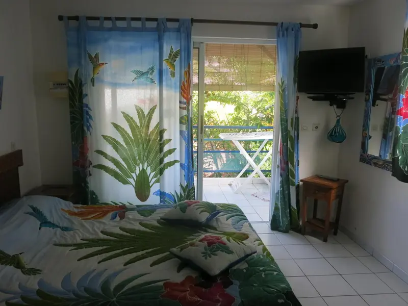 Une chambre lumineuse avec un lit recouvert d'un motif floral et une vue sur une végétation luxuriante.
