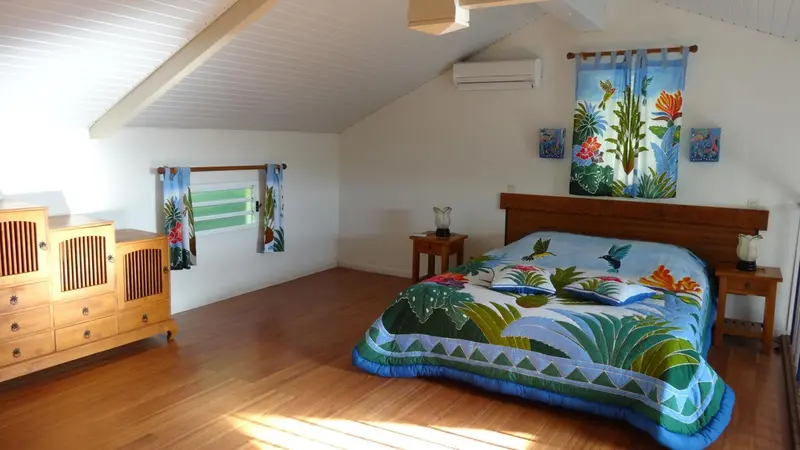 Une chambre lumineuse avec un lit recouvert d'une courtepointe colorée et un meuble en bois.