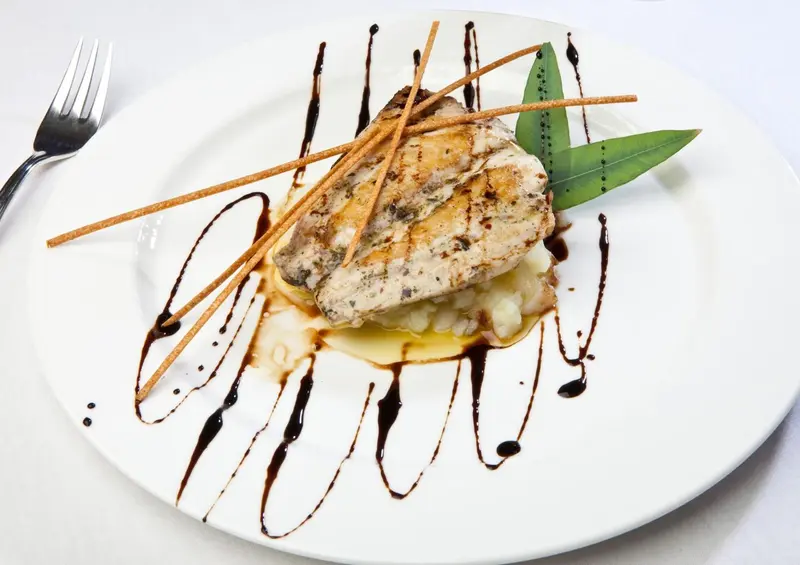 Assiette de poisson grillé décoré de sauce et d'herbes.