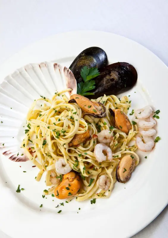 Assiette de pâtes aux fruits de mer présentée sur un lit de coquillages.