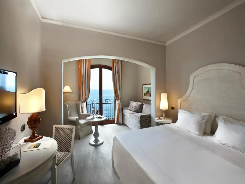 Chambre lumineuse avec un lit blanc et une vue sur la mer.