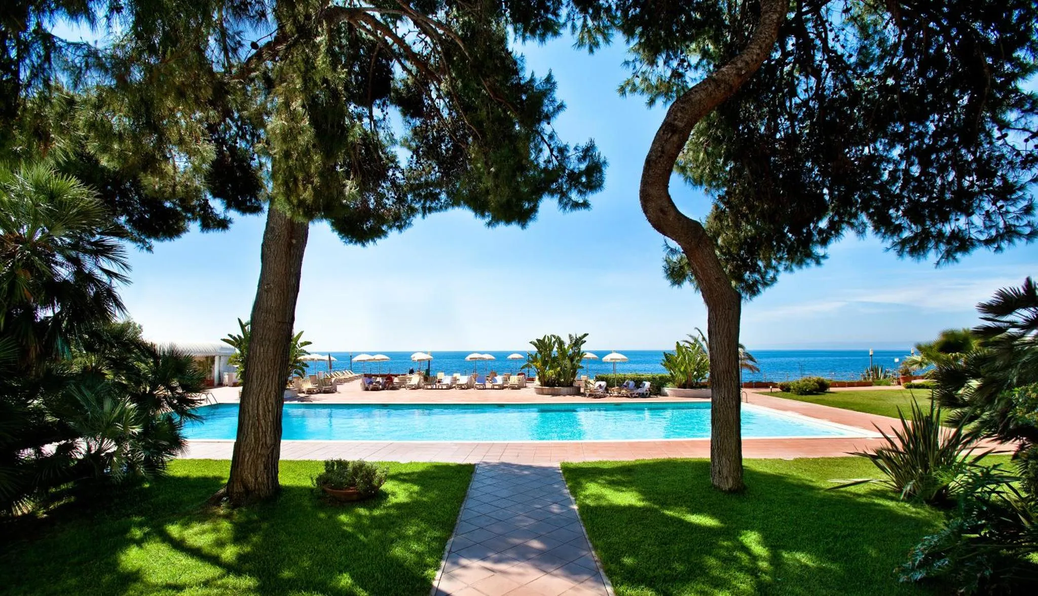 Une piscine rectangulaire bordée d'un jardin verdoyant et d'une terrasse avec des transats.