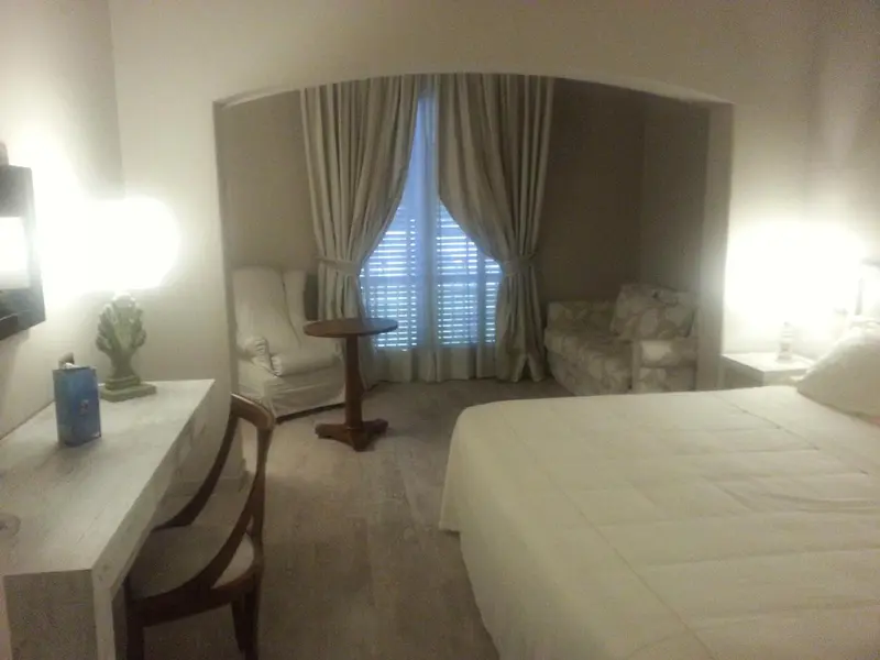 Une chambre lumineuse avec un lit, un bureau et un coin salon près d'une fenêtre.
